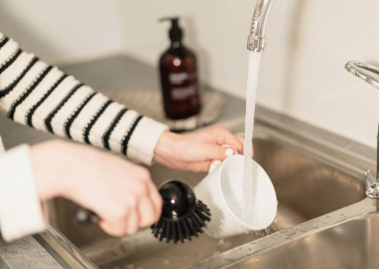 Henkilö huuhtelee astiaa tiskialtaassa